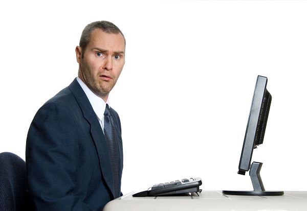 Man in front of computer, looking into camera with a confused expression.