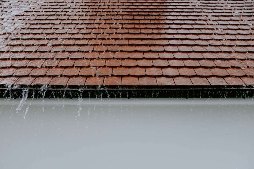 Brick-colored tile roof with rain cascading from it, heading for a barrel to help save rainwater